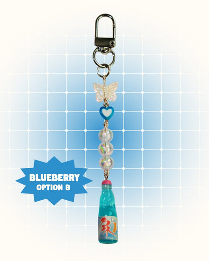 Colorful keychain with blueberry flavor soda on a light blue grid background