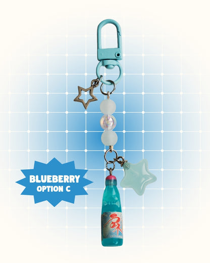Colorful keychain with blueberry flavor soda on a light blue grid background