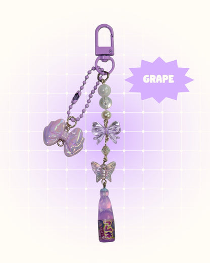 Purple grape soda keychain with decorative elements on a light purple background
