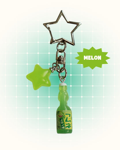 Keychain with star-shaped charm and a small bottle charm on a light green grid background.