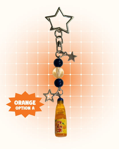 Keychain with orange soda bottle and star charms on an orange gradient background